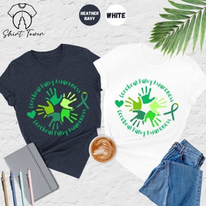 May include: Two t-shirts, one heather navy and one white, with a green handprint design that says "Cerebral Palsy Awareness".
