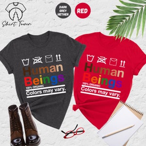May include: Two t-shirts with the words "Human Beings" in rainbow colors and the text "100% Organic Colors may vary."  The t-shirts are in dark heather grey and red.