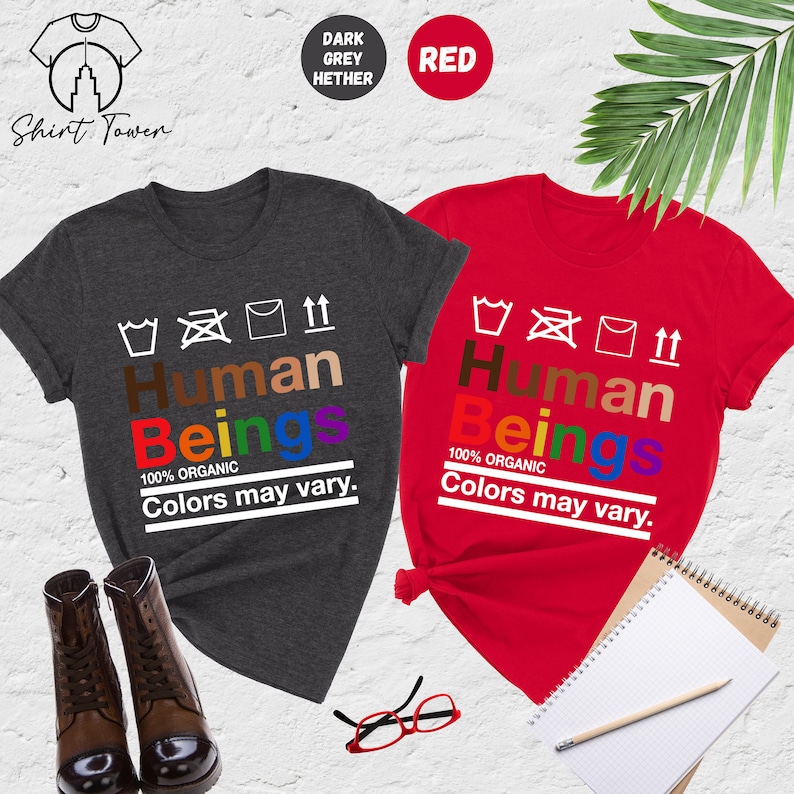 May include: Two t-shirts with the words "Human Beings" in rainbow colors and the text "100% Organic Colors may vary."  The t-shirts are in dark heather grey and red.