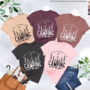 Peut inclure: Cinq t-shirts de diff&eacute;rentes couleurs sur le th&egrave;me du camping. Les t-shirts pr&eacute;sentent un motif blanc d'une tente, d'arbres et d'un croissant de lune avec le texte "Girls - Friends - Fun Camping Crew".