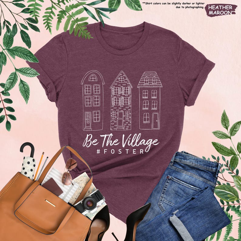 May include: A heather maroon t-shirt with a white graphic of three houses and the text "Be The Village #FOSTERO".
