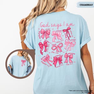 K&ouml;nnte beinhalten: Hellblaues T-Shirt mit einem rosa-wei&szlig;en Design. Das Design zeigt einen Kreis aus Schleifen mit Bibelversen und den Worten "Gott sagt, ich bin".