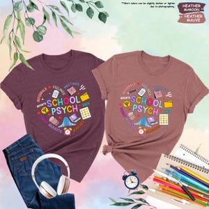 May include: Two heather maroon t-shirts featuring a colourful graphic design that says "School Psych" surrounded by icons representing the work of a school psychologist. The icons include a calendar, a folder, a coffee cup, a laptop, a bell, a pencil, a heart, a brain, and a data file.
