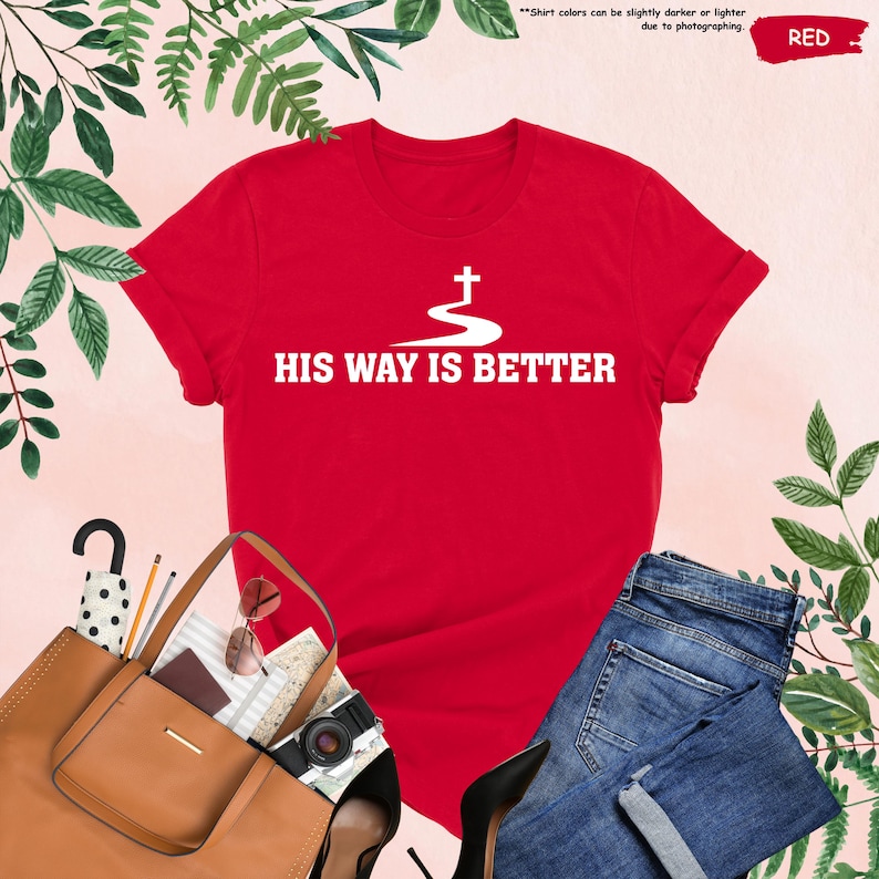 May include: A red t-shirt with the text "HIS WAY IS BETTER" in white, along with a white cross design. The shirt is displayed with a pair of blue jeans, a brown purse, and other accessories.