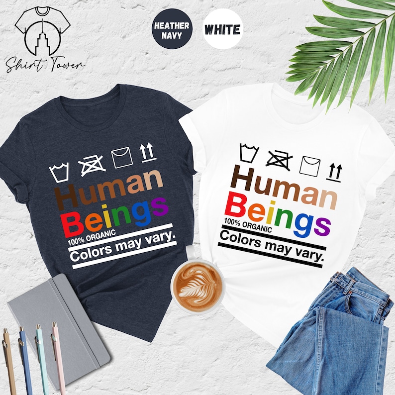 May include: Two t-shirts with the text "Human Beings" in rainbow colors and the words "100% Organic" and "Colors may vary." The t-shirts are in heather navy and white.