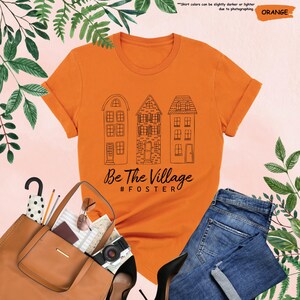 May include: Orange t-shirt with a black graphic of three houses and the text "Be The Village #FOSTER"