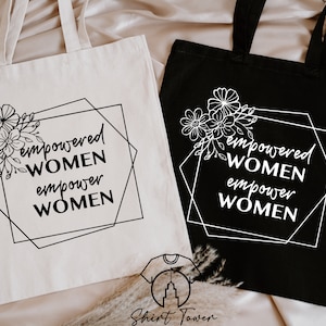 May include: Two tote bags featuring the text "empowered women empower women" within a black geometric frame and a floral design. One bag is white with black text and the other is black with white text.