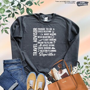 May include: Dark heather grey sweatshirt with white text that reads "Travel Advisor" and lists the responsibilities of a travel advisor, including "stress relieving", "magic making", "wish granting", "flight booking", "dream fulfilling", "advice giving", "cruise booking", "vacation planning", and "Superstar".