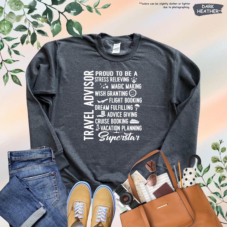 May include: Dark heather grey sweatshirt with white text that reads "Travel Advisor" and lists the responsibilities of a travel advisor, including "stress relieving", "magic making", "wish granting", "flight booking", "dream fulfilling", "advice giving", "cruise booking", "vacation planning", and "Superstar".