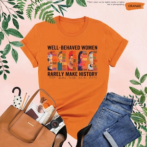 May include: Orange t-shirt with a graphic print of five women's faces and the text "WELL-BEHAVED WOMEN RARELY MAKE HISTORY". The text includes quotes from each woman.