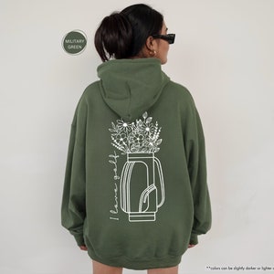a woman wearing a green hoodie with flowers in a vase