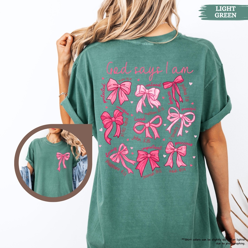 K&ouml;nnte beinhalten: Ein hellgr&uuml;nes T-Shirt mit dem Text "God says I am" auf der R&uuml;ckseite. Der Text ist von rosa Schleifen mit Bibelversen umgeben.