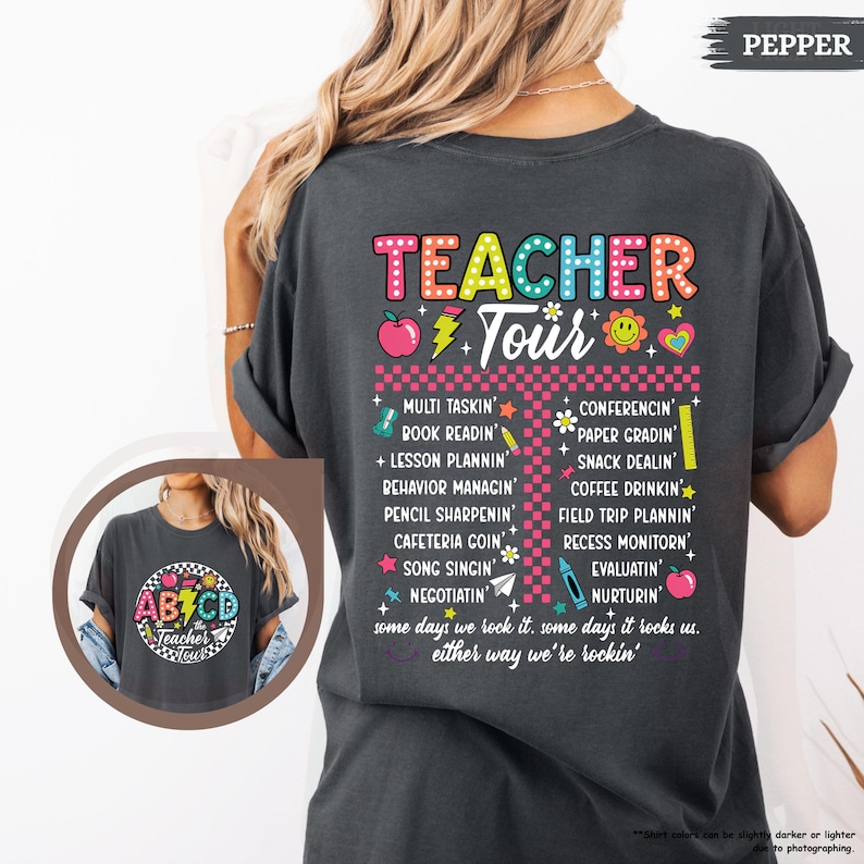 May include: A dark gray t-shirt with the text "TEACHER Tour" in colorful letters. The text is surrounded by various colorful icons and the words "some days we rock it. some days it rocks us. either way we're rockin'."
