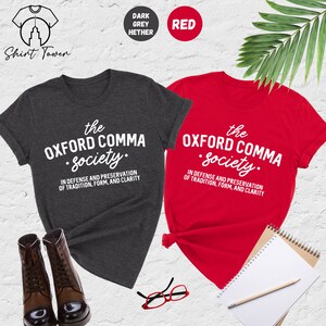 Op de afbeelding: Twee T-shirts, een donker grijs melange en een rode, met de tekst "the OXFORD COMMA Society." en de zin "IN DEFENSE AND PRESERVATION OF TRADITION, FORM, AND CLARITY" erop gedrukt.