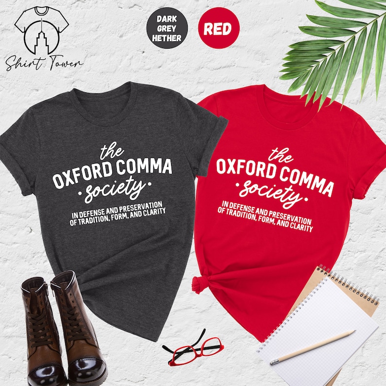 Op de afbeelding: Twee T-shirts, een donker grijs melange en een rode, met de tekst "the OXFORD COMMA Society." en de zin "IN DEFENSE AND PRESERVATION OF TRADITION, FORM, AND CLARITY" erop gedrukt.