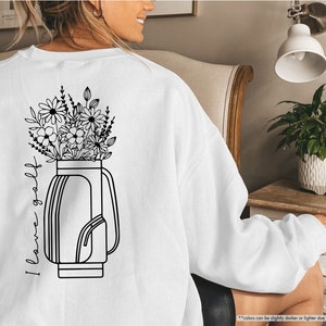 a woman sitting in a chair wearing a sweatshirt with flowers in a vase on it