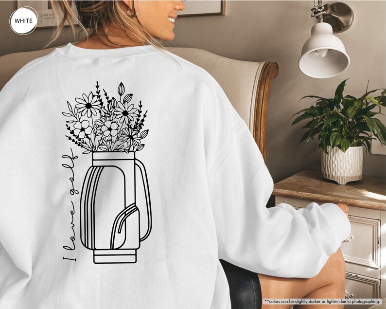 a woman sitting in a chair wearing a sweatshirt with flowers in a vase on it