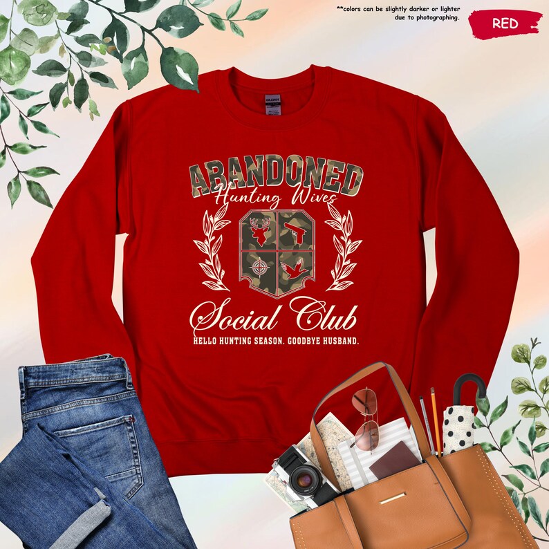 May include: A red sweatshirt with the text "ABANDONED Hunting Wives Social Club" in a camouflage design. The sweatshirt features a crest with hunting-themed graphics and the phrase "HELLO HUNTING SEASON, GOODBYE HUSBAND."