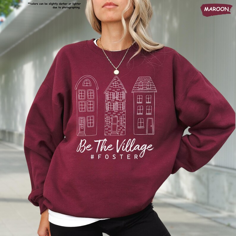 May include: Maroon sweatshirt with a white graphic of three houses and the text "Be The Village #FOSTER"