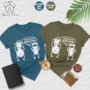 May include: Two t-shirts with a science-themed graphic. The teal shirt says "I think you're overreacting" with a beaker and test tube cartoon. The olive green shirt says the same thing with the same graphic.