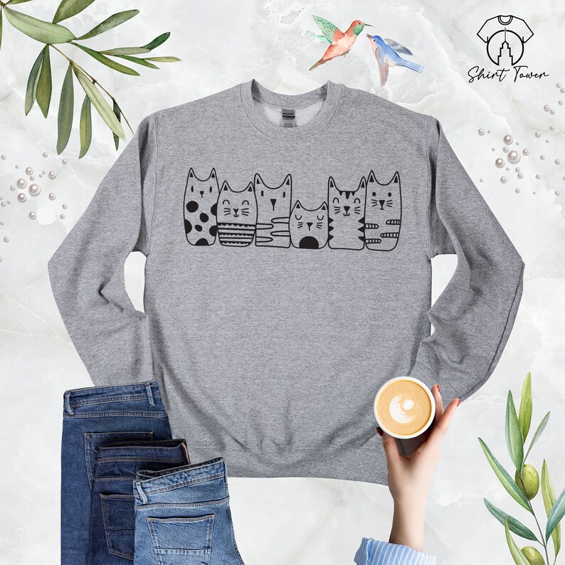 Puede incluir: Sudadera gris con un gr&aacute;fico negro de seis gatos en fila. Los gatos son todos diferentes y tienen caracter&iacute;sticas &uacute;nicas.