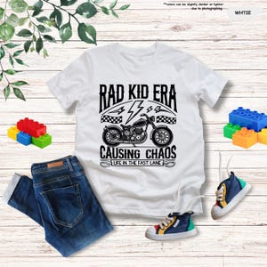 May include: White t-shirt with a black graphic of a motorcycle and the text "Rad Kid Era Causing Chaos Life in the Fast Lane".