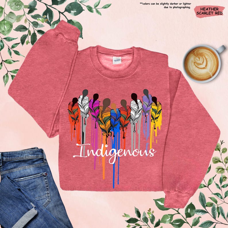 May include: A heather scarlet red sweatshirt with a graphic of a group of people with colorful feathers and the word "Indigenous" in a dripping paint style.