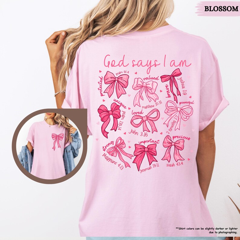 K&ouml;nnte beinhalten: Pinkes T-Shirt mit dem Text "Gott sagt, ich bin" und einem Kreis aus rosafarbenen Schleifen mit Bibelversen. Jede Schleife hat ein Wort wie "gesch&uuml;tzt", "gesch&auml;tzt", "einzigartig", "geliebt", "stark", "wichtig", "kostbar", "m&auml;chtig" und "mutig".