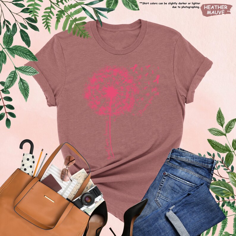 Puede incluir: Una camiseta de color malva con un gran gr&aacute;fico de diente de le&oacute;n rosa. La imagen incluye vaqueros azules, un bolso marr&oacute;n y tacones altos negros. El texto "HEATHER MAUVE" es visible. El color de la camiseta puede variar.