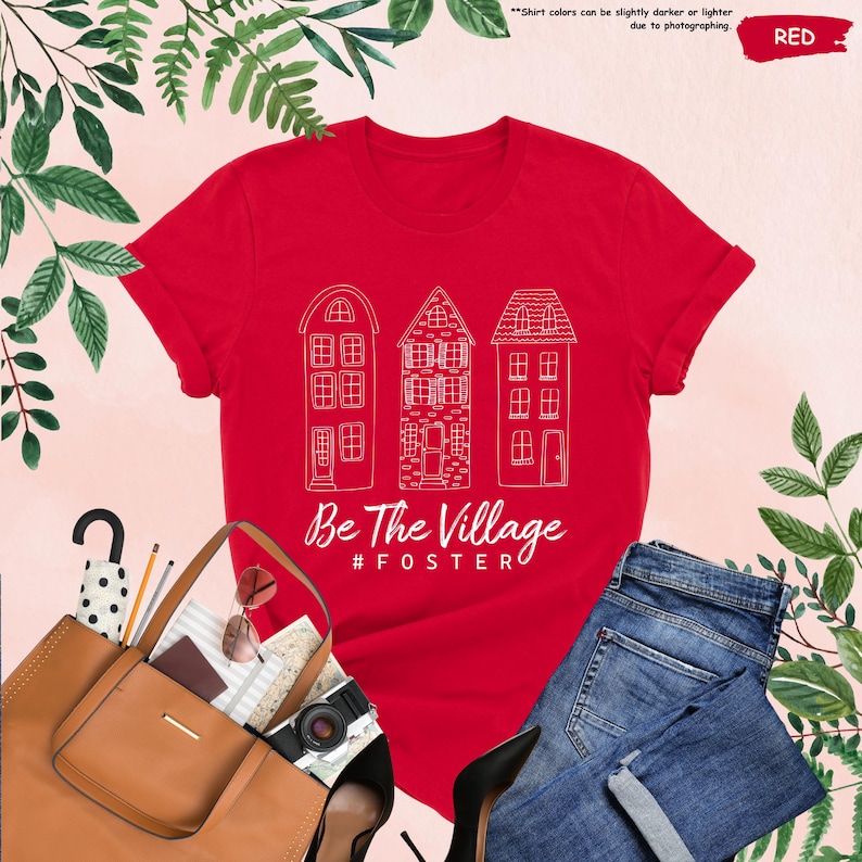 May include: Red t-shirt with a white outline of three houses and the text "Be The Village #FOSTER"