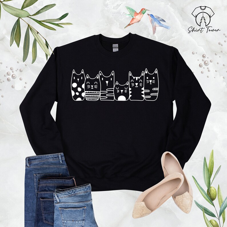 Puede incluir: Sudadera negra con un gr&aacute;fico blanco de cinco gatos en fila, cada uno con un patr&oacute;n diferente. Los gatos miran todos hacia la derecha.
