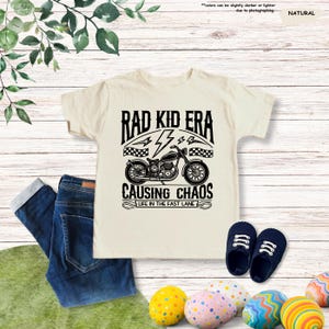 May include: A white t-shirt with a black graphic of a motorcycle and the text "Rad Kid Era", "44", "Causing Chaos", and "Life in the Fast Lane".
