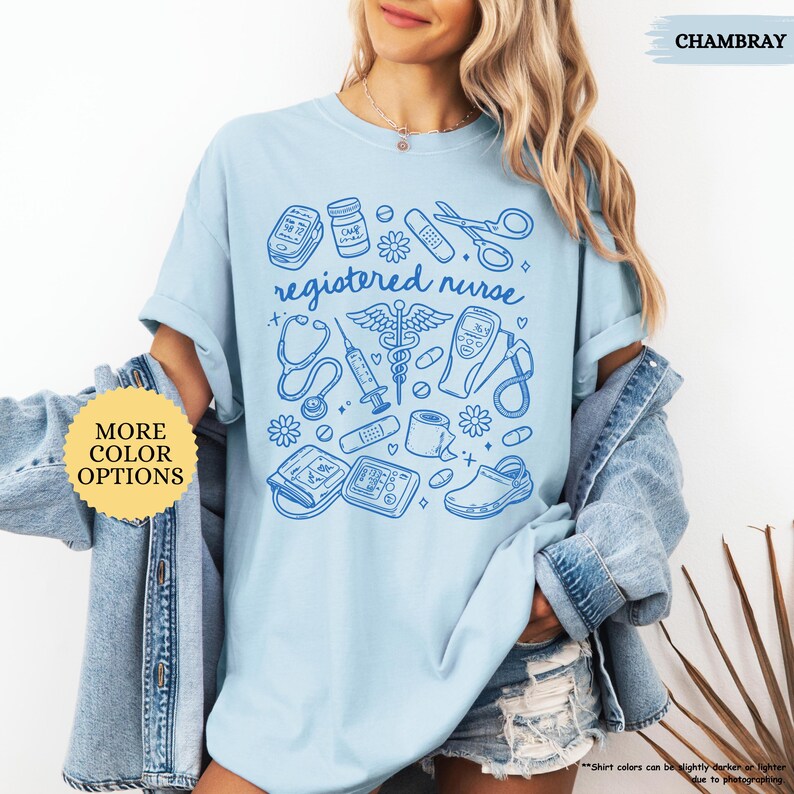 May include: Light blue t-shirt with a blue graphic of medical tools and the words "registered nurse." The design includes a stethoscope, syringe, and other medical equipment. The shirt has short sleeves and a crew neck.