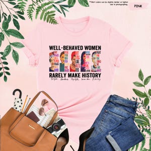 May include: Pink t-shirt with a graphic print of famous women and the text "Well-Behaved Women Rarely Make History". The graphic includes portraits of Frida Kahlo,  Audre Lorde, Maya Angelou, Ruth Bader Ginsburg, and  RBG's quote "Fight for the things that you care about."