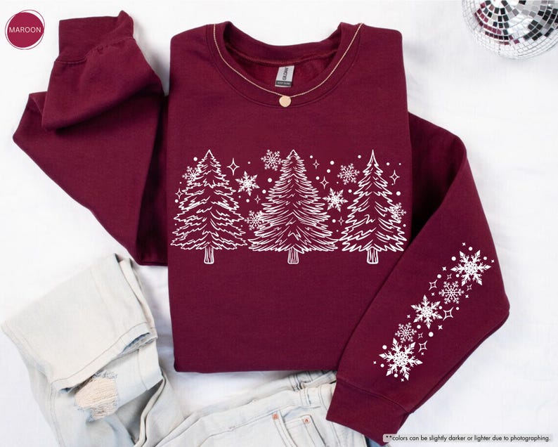 May include: A maroon sweatshirt with a white design of stylized Christmas trees and snowflakes. The design is on the front of the sweatshirt and the sleeves have a line of snowflakes.