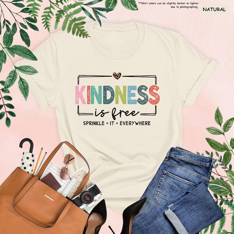 May include: A white t-shirt with the text "KINDNESS is free" in colorful letters with a heart above the text. The text "SPRINKLE IT EVERYWHERE" is below the main text.