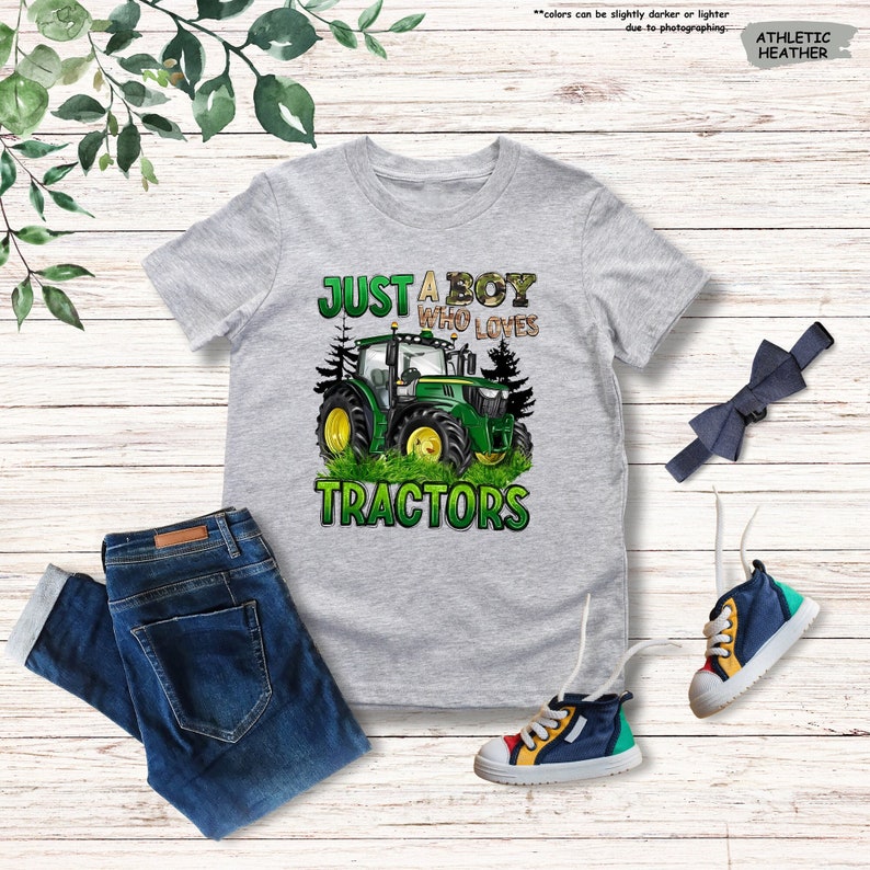 May include: A gray athletic heather t-shirt with a green and yellow tractor graphic and the text "JUST A BOY WHO LOVES TRACTORS." The image also includes blue jeans, a bow tie, and colorful sneakers.
