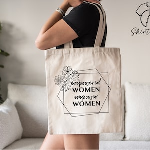 May include: A white canvas tote bag with black text and floral design. The text reads "empowered women empower women".
