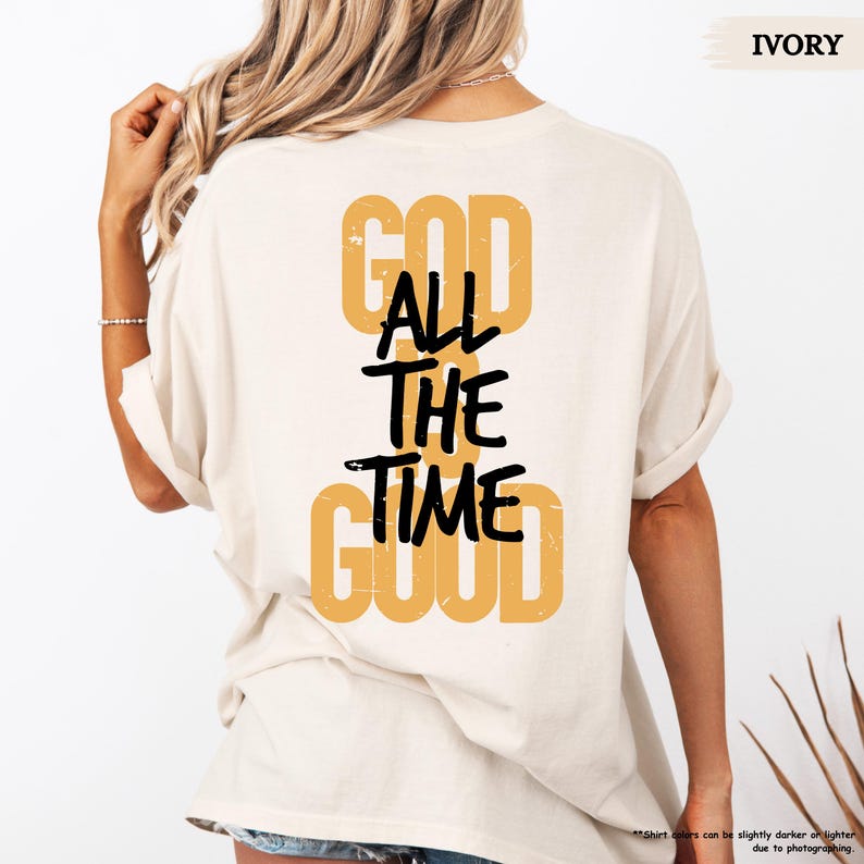 May include: Ivory-colored t-shirt with the text "GOD ALL THE TIME GOOD" in a combination of mustard yellow and black. The shirt's back is visible, with the text arranged vertically.