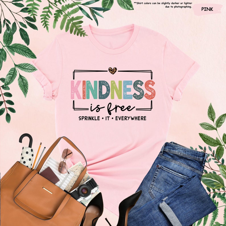 May include: Pink t-shirt with the text "KINDNESS is free - SPRINKLE IT EVERYWHERE" in colorful letters. The shirt has a small heart with leopard print on the top left corner.