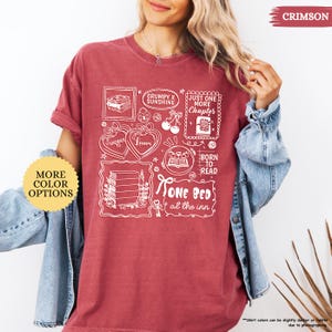 May include: Crimson-colored t-shirt with a white graphic design featuring book-themed illustrations and text. The design includes phrases like "Grumpy x Sunshine," "Just One More Chapter," and "Born to Read." The shirt has a relaxed fit.