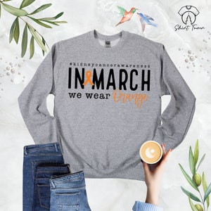 Puede incluir: Sudadera gris con el texto "#kidneycancerawareness IN MARCH we wear Orange" y una cinta naranja.