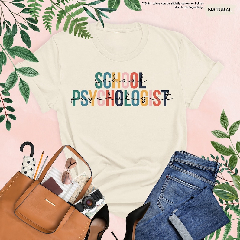 Op de afbeelding: Een wit T-shirt met de tekst "SCHOOL PSYCHOLOGIST" in regenboogkleuren. De tekst is in een gestileerd lettertype.
