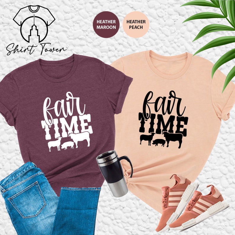 May include: Two t-shirts with the text "fair time" and a graphic of farm animals. The shirt on the left is heather maroon and the shirt on the right is heather peach.