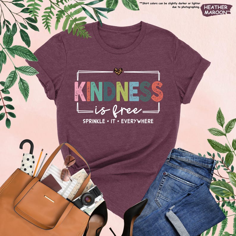 May include: A heather maroon t-shirt with the text "KINDNESS is free" in colorful letters with a distressed look. The text "SPRINKLE IT EVERYWHERE" is below the main text.