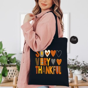 Pode incluir: Sacola tote preta com o texto "So very thankful" em letras coloridas e cora&ccedil;&otilde;es.