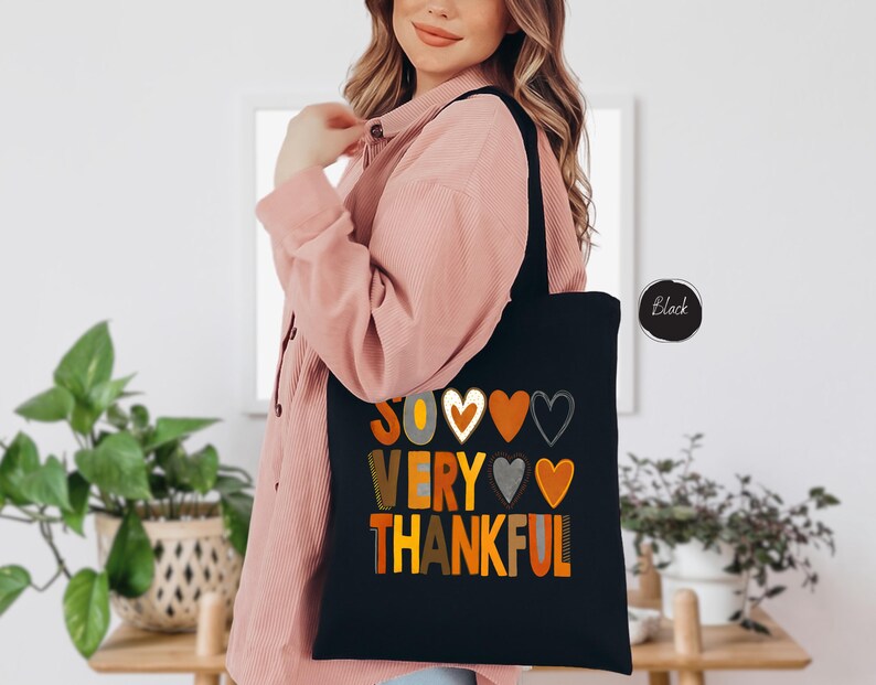 Pode incluir: Sacola tote preta com o texto "So very thankful" em letras coloridas e cora&ccedil;&otilde;es.