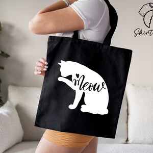 Op de afbeelding: Een zwarte tote bag met een wit silhouet van een kat en het woord "Meow" in een cursief schrift.