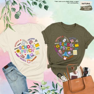 May include: Two t-shirts featuring a graphic design representing the work of a school psychologist. The design incorporates a heart shape with the words "School Psych" at its centre and various icons and text associated with the profession, such as "reports", "meetings", "data", "parent requests", and "deadlines". One shirt is a light beige colour and the other is a dark green colour.