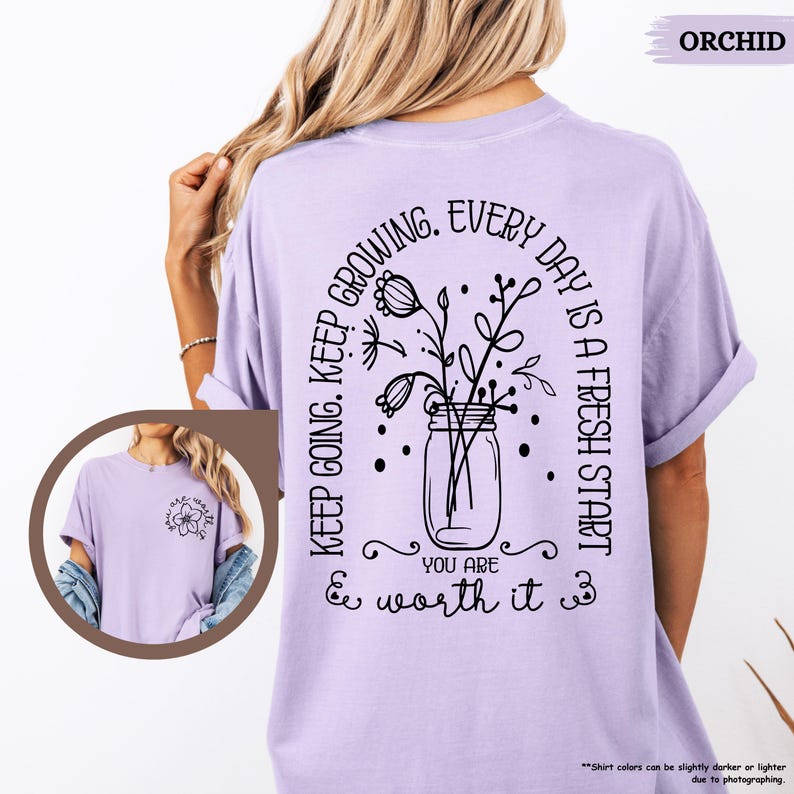 May include: A lavender t-shirt with a black graphic design featuring a jar of flowers and the text "Keep going. Keep growing. Every day is a fresh start. You are & worth it."